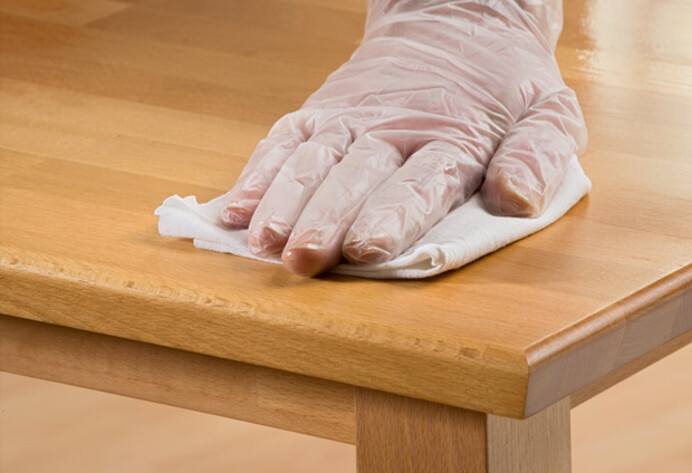 Hand mit Handschuh ölt Holztisch ein