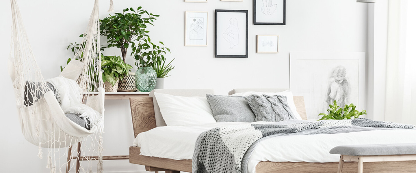 Stilvoll eingerichtetes Schlafzimmer mit einem Holzbett, mit weißer Wandfarbe, Bildern, einer Hängeschaukel