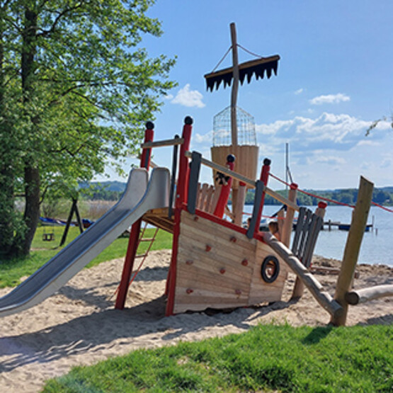 Spielplatz von Spielplatzbauer Mehrtens in der Form eines Piraten Schiffswracks mit Rutsche an einem Seeufer