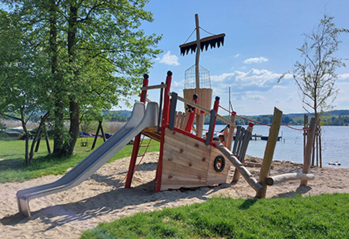 Spielplatz von Spielplatzbauer Mehrtens in der Form eines Piraten Schiffswracks mit Rutsche an einem Seeufer