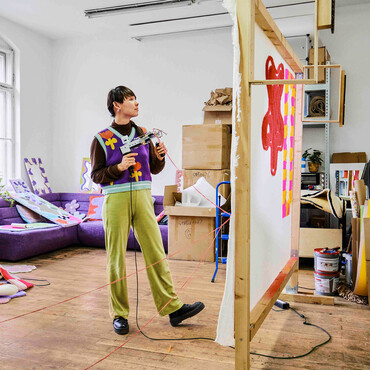 Zeyu Cheng steht mit Tufting-Pistole in der Hand vor einer Leinwand