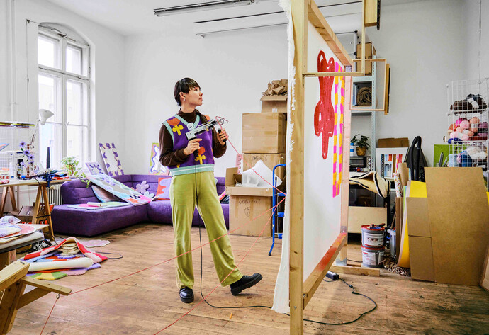 Zeyu Cheng steht mit Tufting-Pistole in der Hand vor einer Leinwand