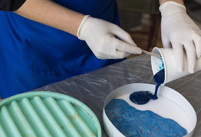 Frau mit Plastik-Handschuhen gie&szlig;t blaue Farbe auf einem Becher in eine Schale