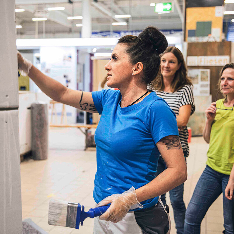 Frau streicht Wand, andere Frauen schauen zu