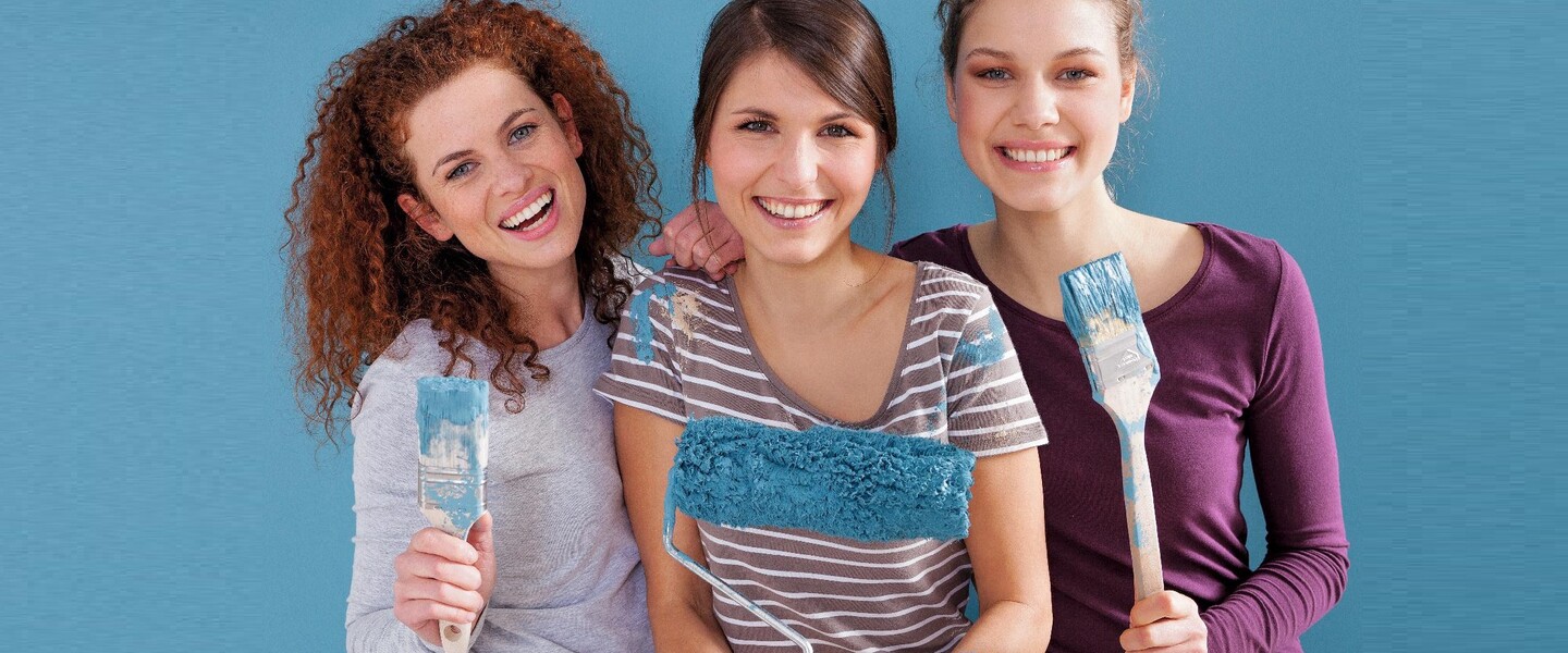 Drei Frauen haben Pinsel und Farbrollen in der Hand
