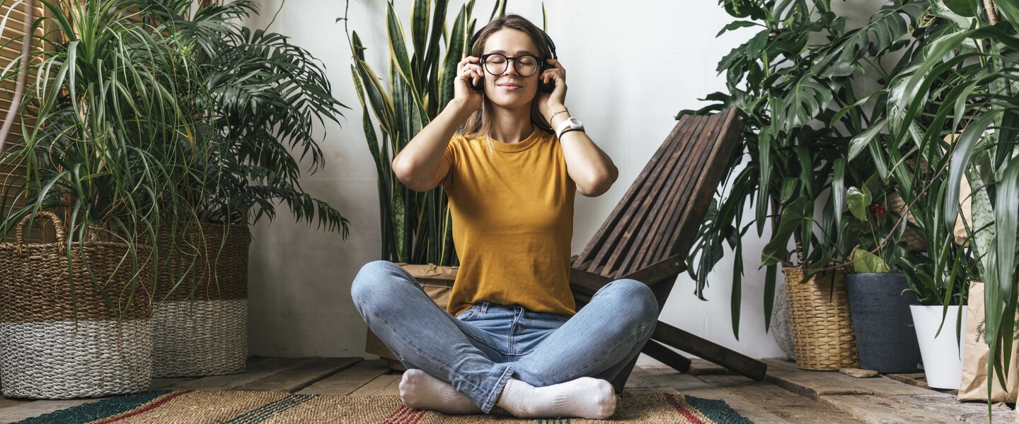 Frau sitzt zwischen Zimmerpflanzen auf Teppich und hört Musik