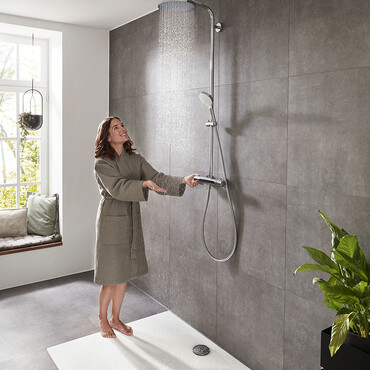 Frau mit Bademantel steht unter bodenebener Dusche und stellt das Wasser an