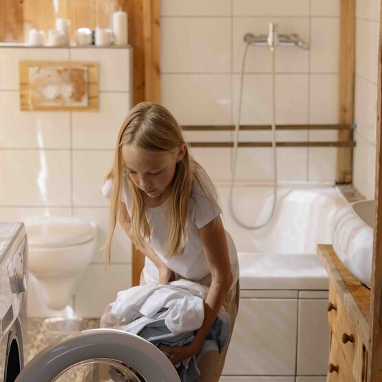 Mädchen befüllt Waschmaschine im Badezimmer