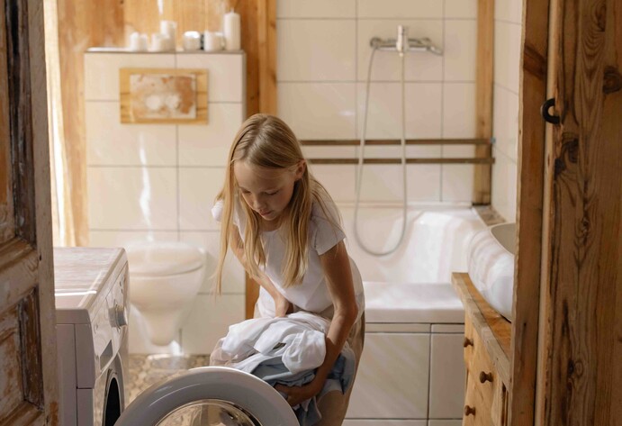 Mädchen befüllt Waschmaschine im Badezimmer